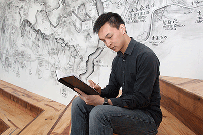 Sitting beside a BAMPFA mural project by renowned Chinese artist Qui Zhijie, senior Andrew Wong does some journaling. (UC Berkeley photo by Brittany Murphy)