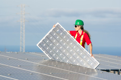 a worker in a green hardhat carries a solar panel for installation