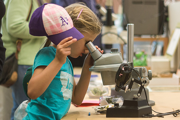 Young girl looking into microscope at Cal Day