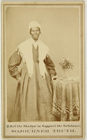 old, weathered photograph of Sojourner Truth standing next to a table.