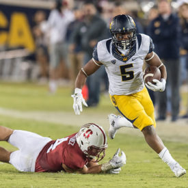 A Cal football player runs with ball and evades a tackle from a player on the other team. 