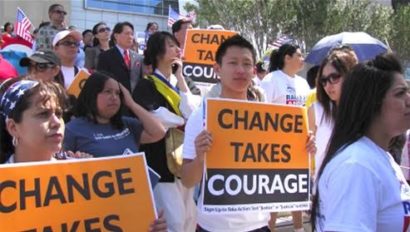 A photo of a crowd of people standing outside in protest with signs that read "Change takes courage".