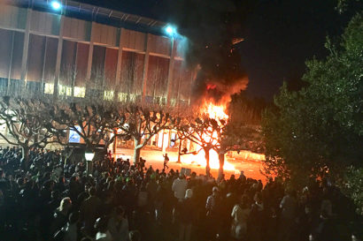 A crowd of protesters surrounds a pillar of flames on Sproul Plaza at UC Berkeley