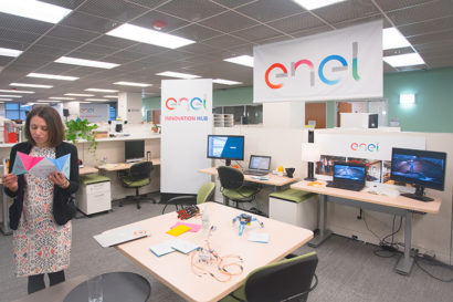 A photo of an office with a woman standing reading a paper on the left hand side. There are many signs that read "enel" suggesting the name of the company.