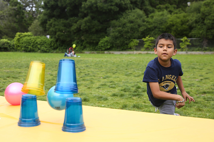 kid throwing ball knocking over cups