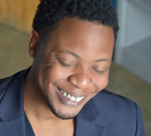 An up close photo of a man smiling with his eyes closed, presumably looking down. 