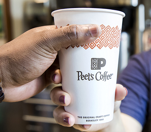 A close-up of a hand holding a Peet's Coffee cup.