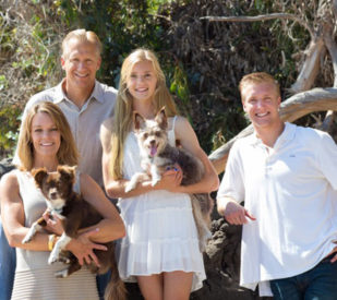 A photo of family members smiling outside, two of which are holding dogs. 