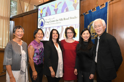 A photo of five women and a man standing side by side, smiling, indoors in front of a projector board with a slide on it that reads "Tang Center for SIlk Road Studies".