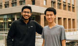 A photo of Zuhayeer and Jimmy, side by side smiling, outside in front of a building. 