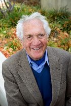 Emeritus professor John Letiche, smiling and seated outdoors.