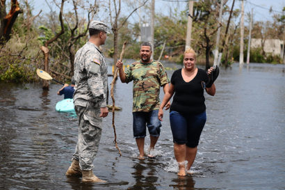 A photo of a National guard standing by a civilian couple outside in a foot of water.
