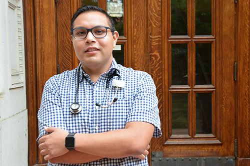 Juan Medina-Echeverria, a public health major, stands with his arms crossed, wearing a stethoscope around his neck.