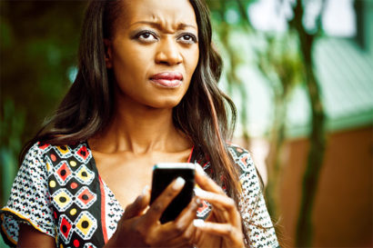 A women holds a phone as she gazes in another direction with a look of confusion and disgust on her face. 