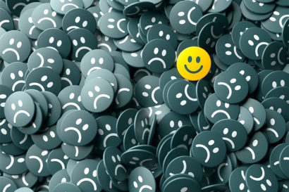 Amongst a pile of sad, black frowning face emojis sits a single, yellow smiling face emoji. 
