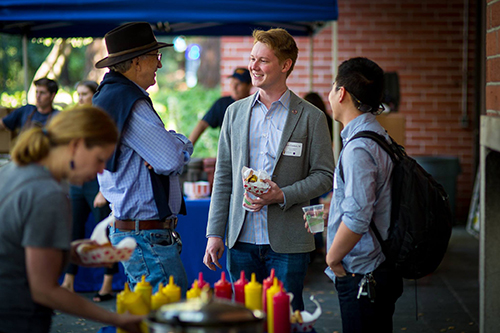 Three people chatting and holding food at the GBO mixer.