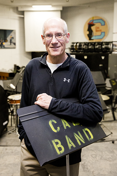 Bob Calonico, director of bands at UC Berkeley, stands holding a "Cal Band" music stand in a rehearsal room.