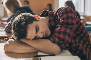 A student rests their head on a desk, symbolizing the impact of social jetlag and misaligned schedules on academic performance.