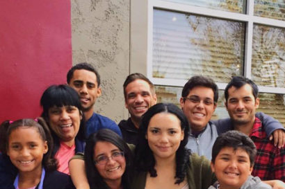 A group of nine people of varying ages stand with their arms around each and smile at the camera. 