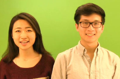 A woman and a man pose in front of a green-screen.