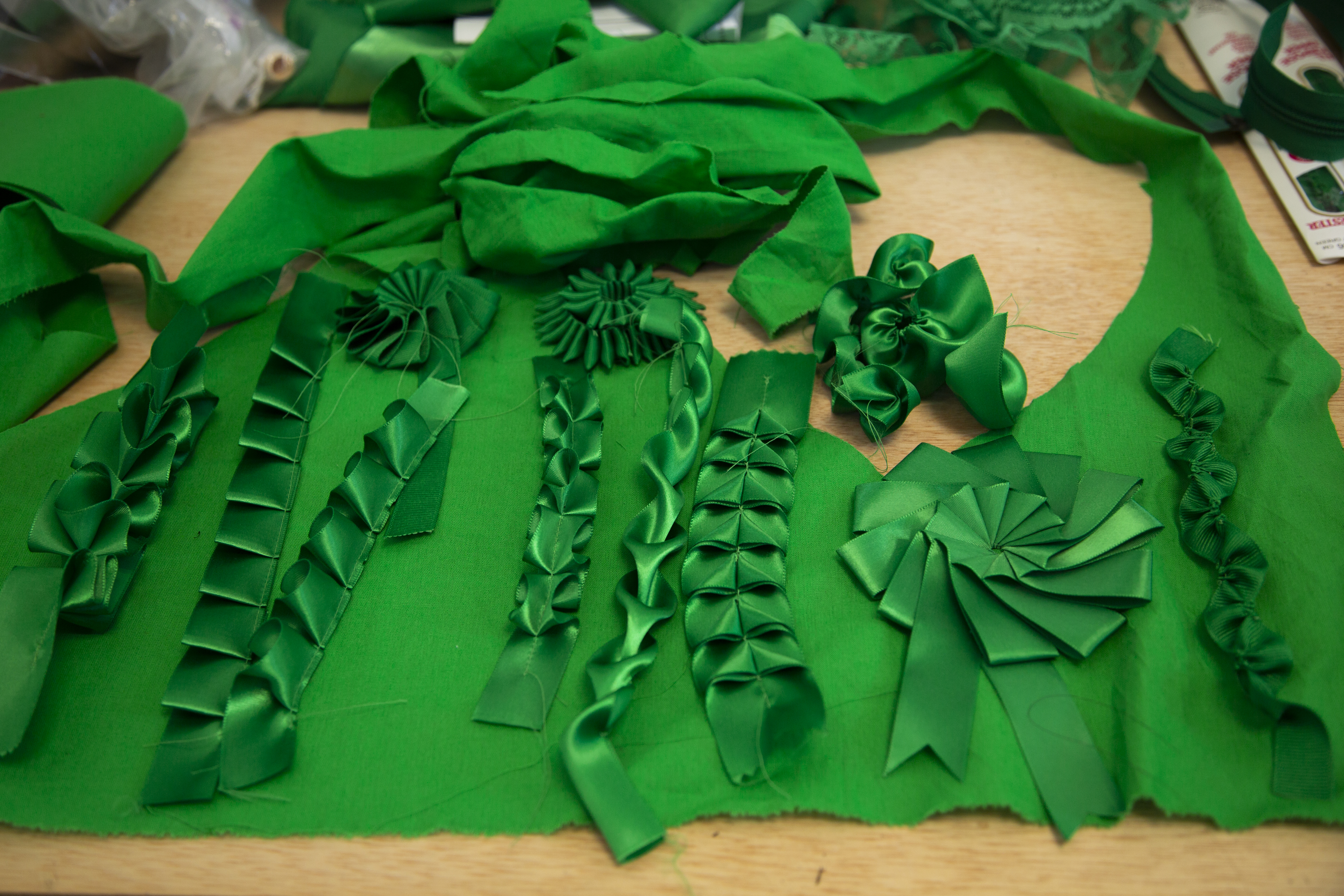 An array of ribbons, trim and fabric swatches in matching chroma key green. Syjuco produced small embellished samples before deciding which methods she would use in her final artwork.