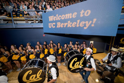 The Cal Band and Dance Team gathers underneath a digital sign that reads "Welcome to UC Berkeley!" inside Haas Pavilion during convocation