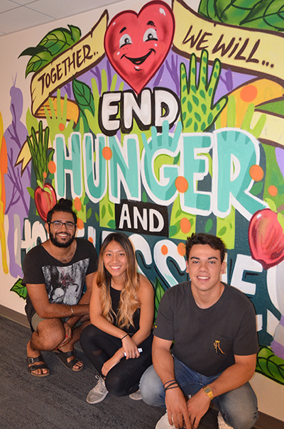 Student leaders involved with CalFresh and the food pantry pose next to a mural that says "Together we will end hunger and homelessness."