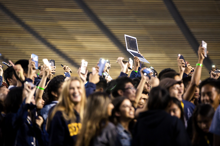 students hold up cellphones and laptops