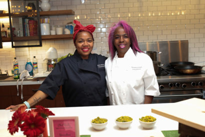 Sicily Johnson stands next to her mother Bernadine Sewell in the kitchen of their restaurant Pinky and Red's. Sewell's hair is dyed a vibrant shade of pink, while Johnson sports a red bandana on her head.