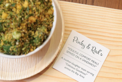 A baked vegetable dish sitting on a wood table. Next to the dish is a small card with Pinky and Red's information displayed