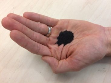 A close-up of a man's hand holding a black sandy substance. 