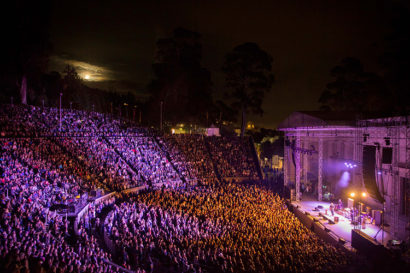 Concert goers are bathed in purple light during a live, nighttime music concert at the Greek Theatre on UC Berkeley's campus