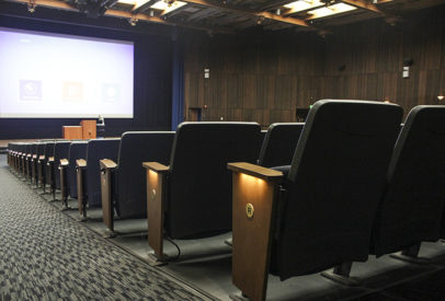 Rows of chairs face a projector in the newly renovated auditorium in Wheeler Hall. On the outside of the row, small lights illuminate the aisles towards the center lectern.