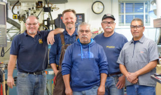 A photo of the physics crew consisting of five men, four of which are smiling, while the middle individual is simply looking at the camera.