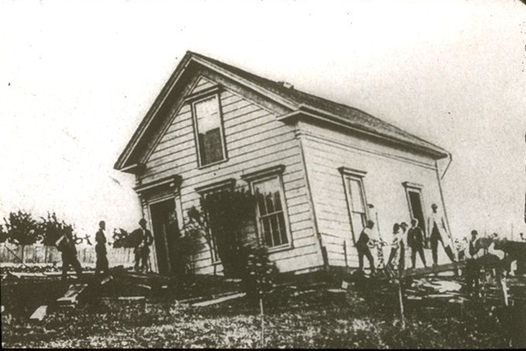 A wooden house is tilted off its foundation