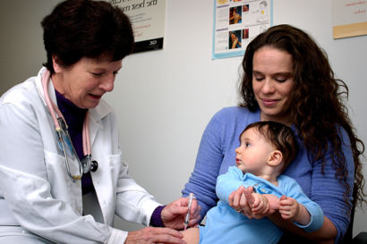 A woman holds an infant on her lap while they receive a vaccine from a medical provider. 