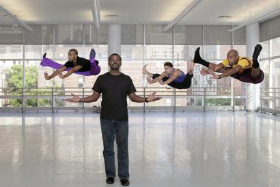 Robert Battle holding his hands up with three dancers leaping into the air behind him