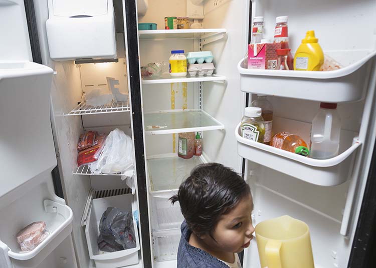 a child in front of a mostly empty refrigerator