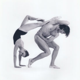 Erika doing a handstand with her legs on a man's back, who isn't wearing clothes