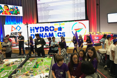 Students ages 9 to 14 gather around a LEGO table