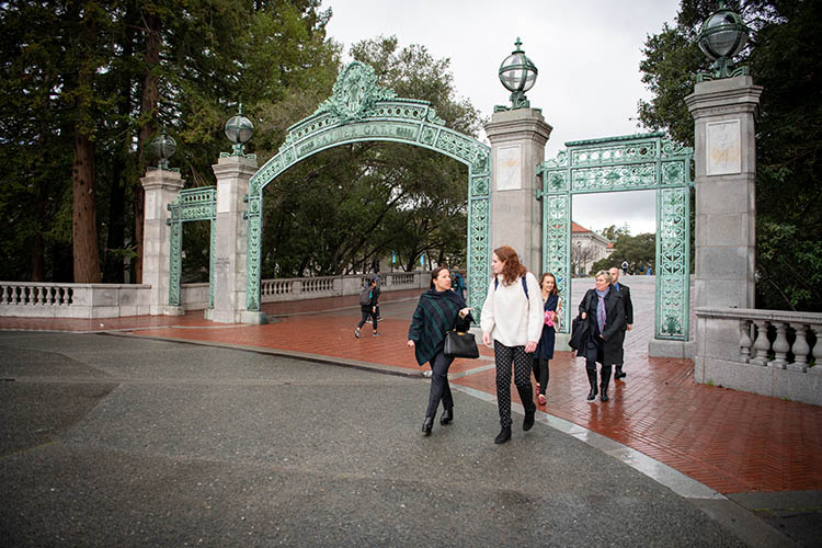 a woman and a student walk through sather gate