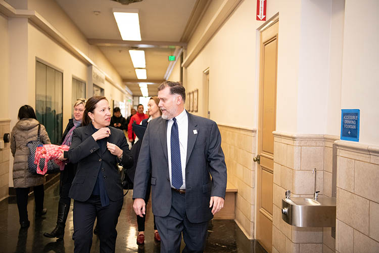 a woman and a man walk and talk down a hallway