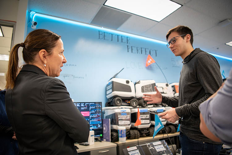 a woman talks to a young man in front of robots