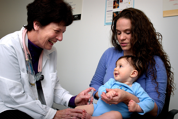 A mother holds a baby while a doctor administers a shot