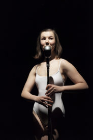 a woman standing at a microphone wearing a white bathing suit