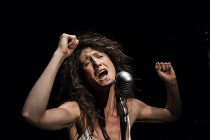 woman singing at microphone with her eyes closed and closed hands in the air