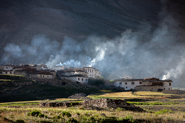 Photo shows houses on a hillside with smoke emerging from smokestakcs