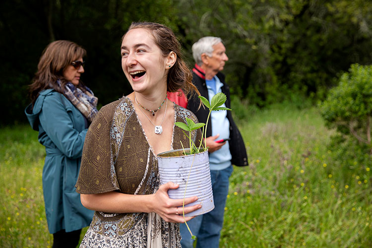 Skye Michel laughs and holds a strawberry plant outside during the alternative graduation ceremony