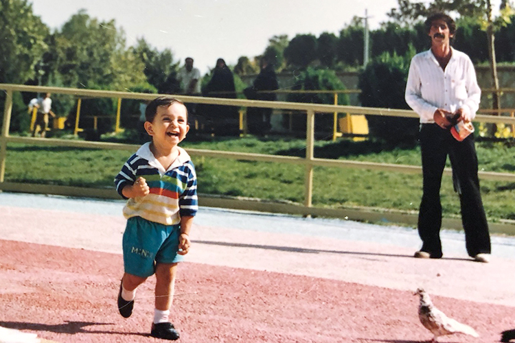 3-year-old Pouya runs in a park laughing with his dad in the background