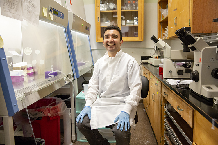 a portrait of pouya amin sitting on a chair in a lab